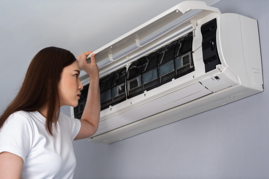 Air conditioner not cooling as a woman checks and inspects the indoor AC unit filter while troubleshooting cooling issues before calling for repair