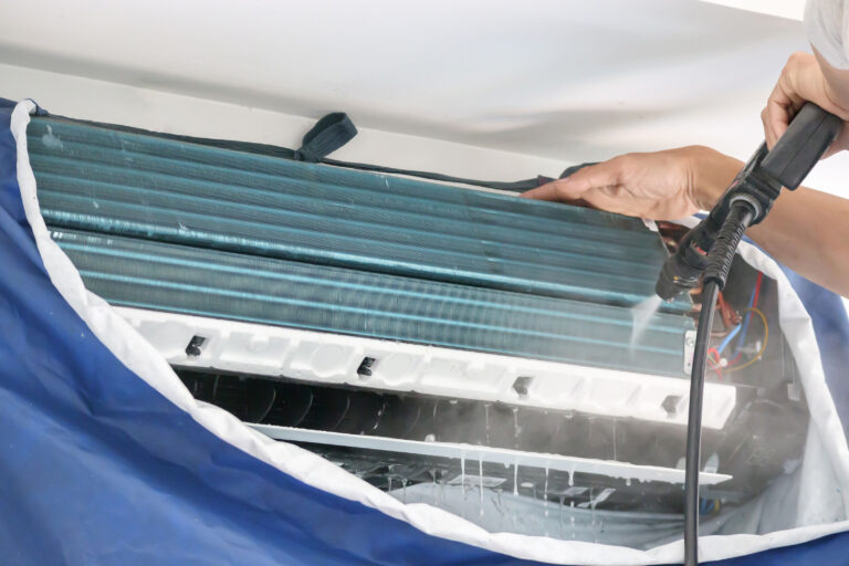 Technician performing an aircon chemical wash on an indoor unit, illustrating common myths about chemical washing for air conditioners in Singapore.