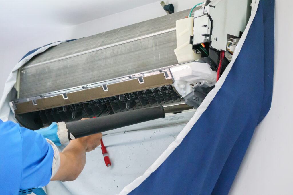 Technician cleaning indoor air conditioner unit with tools, illustrating step-by-step professional aircon servicing process by Peakcool.